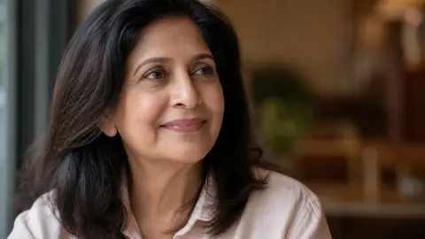 South Asian woman in her mid-fifties with a gentle smile, soft natural light