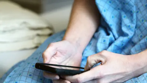 Patient in a hospital gown holding a smartphone